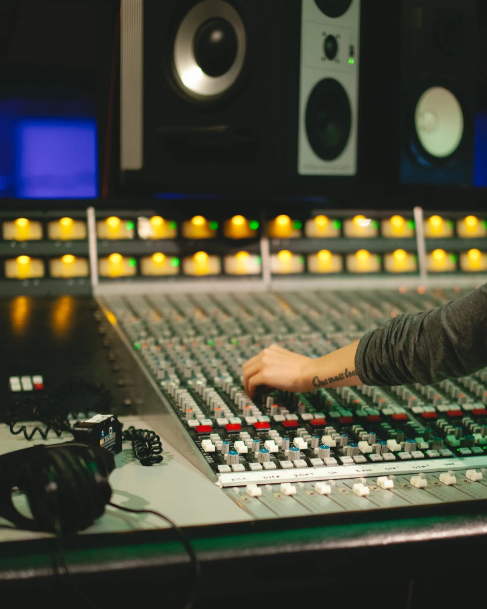 Hands on a large mixing console in a studio, monitors above
