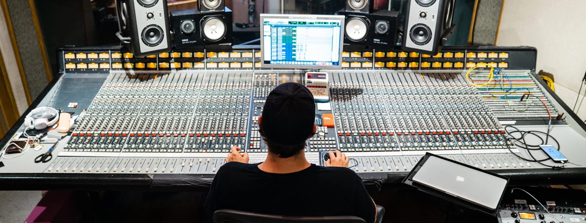 A studio control room seen from behind the engineer, large console and monitors